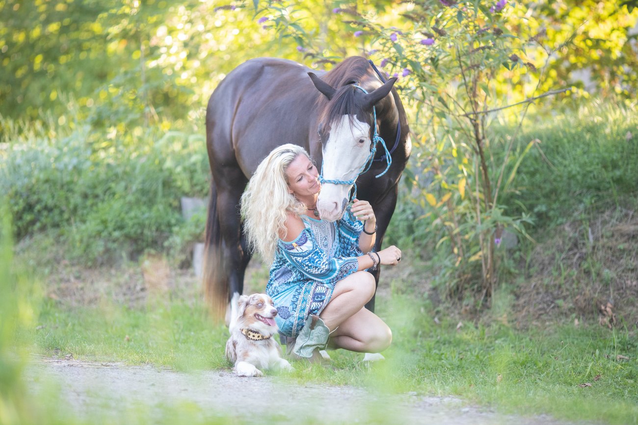Caro kniet zwischen ihrem Pferd und ihrem Hund im Grünen
